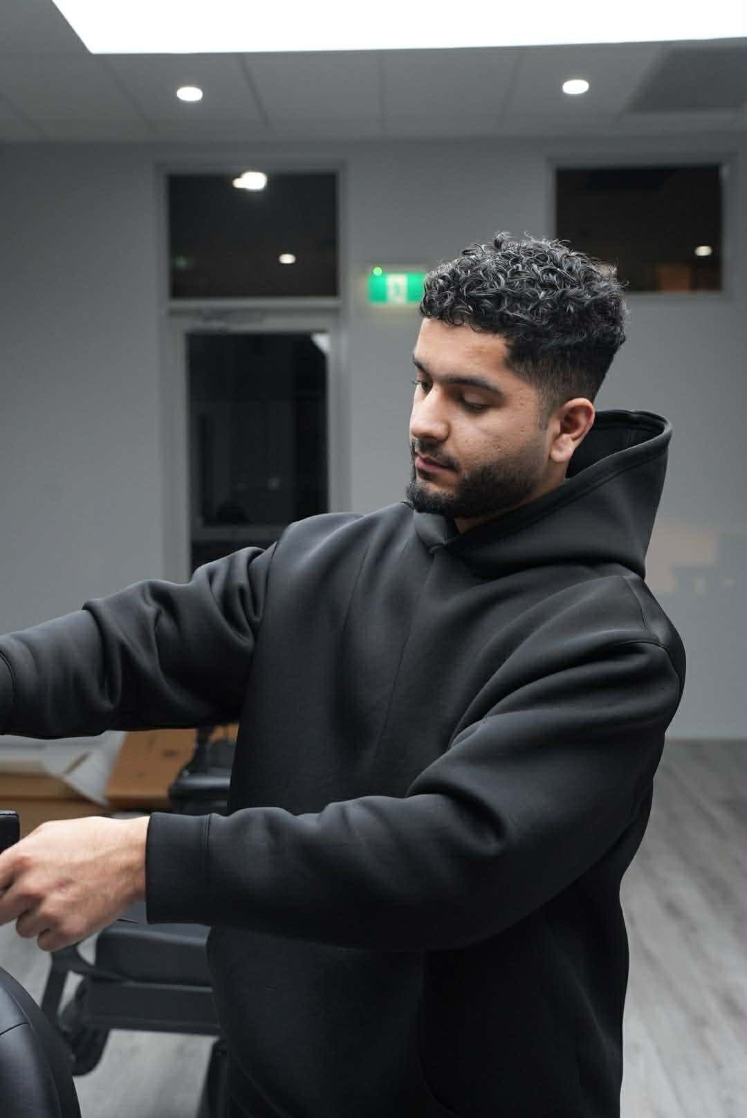 Man in black hoodie standing in modern office space with gray walls and recessed lighting